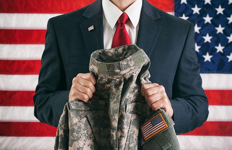 photo of man in suit in front of american flag, holding uniform